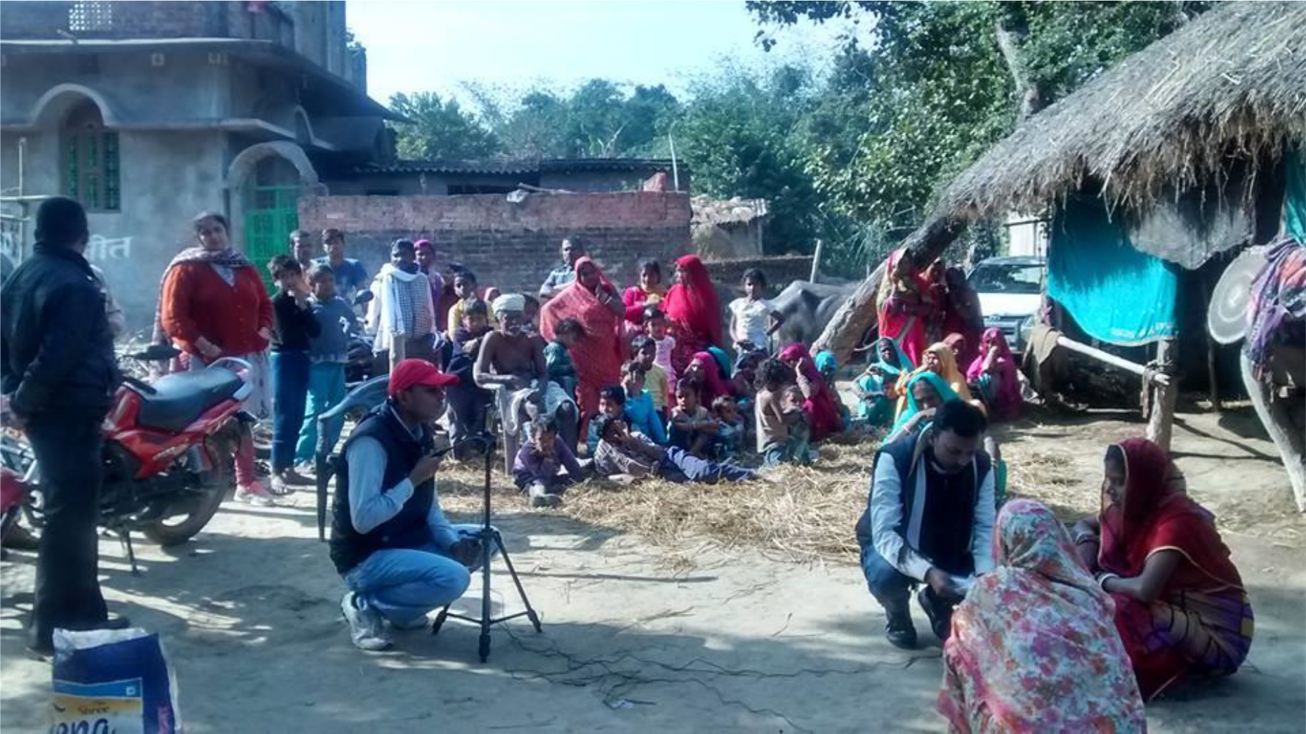 The image shows a scene from the village where some professionals are shooting a video of villagers. A big crowd of villagers is looking at this process.