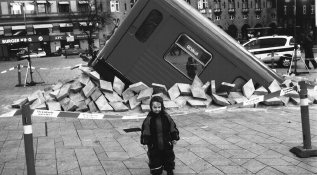 A 2001 April Fool's Day prank in Denmark, regarding Copenhagen's new subway. It looks as if one of its cars had an accident and had broken through and surfaced on the square in front of the town hall. In reality, it was a retired subway car from Stockholm, Sweden, cut obliquely, with the front end placed onto the tiling and loose tiles scattered around it. The sign in the window refers to Gevalia coffee, which is known for its ads featuring vehicles popping up, with a tagline such as “Be ready for unexpected guests.”