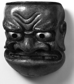 Kyōgen mask of the character Buaku. The faintly comical demon mask of Buaku is the Kyōgen version of the Nō theater mask of Beshimi. Both the characterization and stylized carving of this mask reflect the original prototype. The mask is carved from a single piece of cypress, with the features in high relief. The surface has been treated with a layer of gofun that has been painted a deep flesh color. The folds of flesh around the eyes, cheeks, brow, and mouth have been accentuated by the creases painted in a deep red color with additional highlights in black ink. Black ink, applied in firm yet sensitive lines, has also been used for the hair, eyebrows, mustache, and whiskers. The eyeballs have had gold leaf applied, with the edges emphasized by lines of ink accentuated by red painted rims. This follows the Nō theater tradition of coloring the eyes of a demon red and gold.