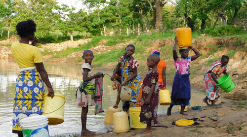 Women and children filling water from a pond in plastic barrels and buckets, and apparently exchanging some chat.