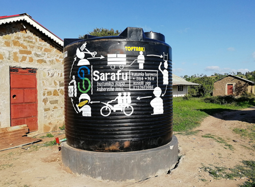 A plastic water tank mounted on a cemented platform. There is graffiti on the water tank with Sarafu written at its centre and a phone number on its right.