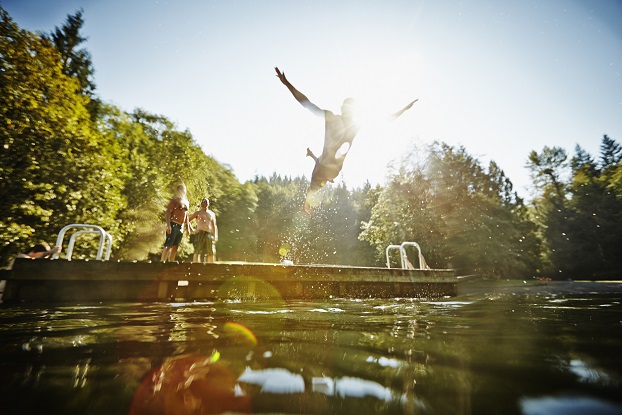 A picture shows a man diving off a dock. Two friends are standing on the dock.