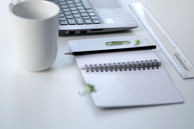 A picture shows a notepad, a pencil, a pen, a cup, a ruler, and a laptop neatly placed on a white surface.